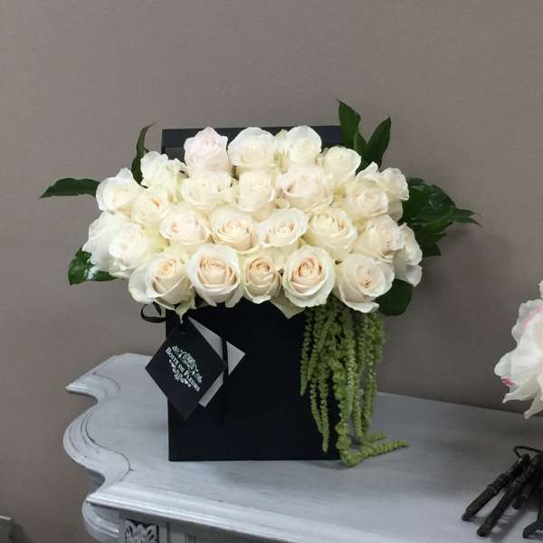 Cream rose arrangement in a black box with trailing greenery