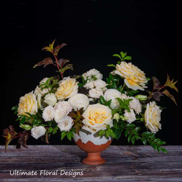 Cream and pale yellow roses arranged in a terracotta pedestal vase