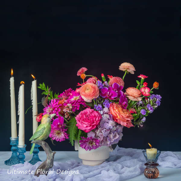 Colorful flower arrangement in a white vase with candles and a bird figurine