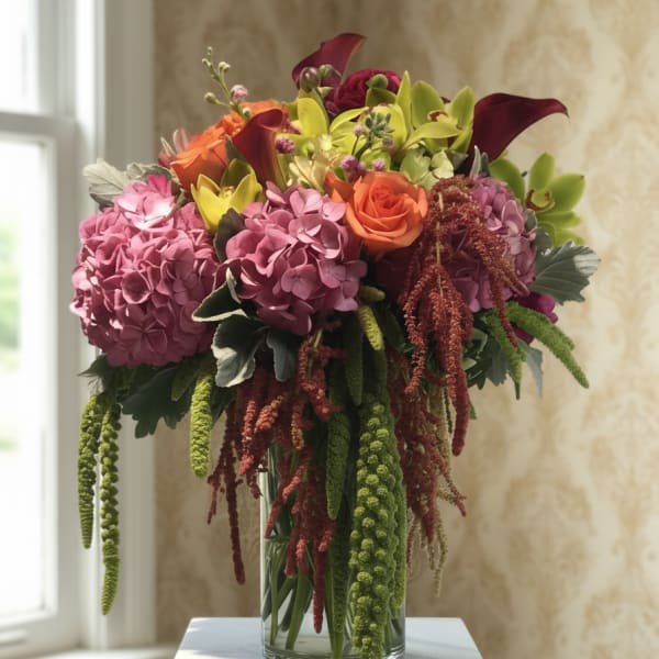 Bouquet of pink hydrangeas, orange roses, and calla lilies in a glass vase