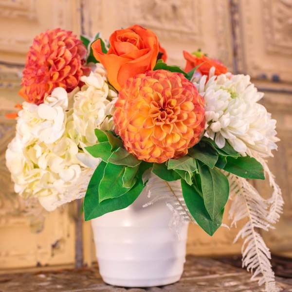 Orange and white floral arrangement in a white pot