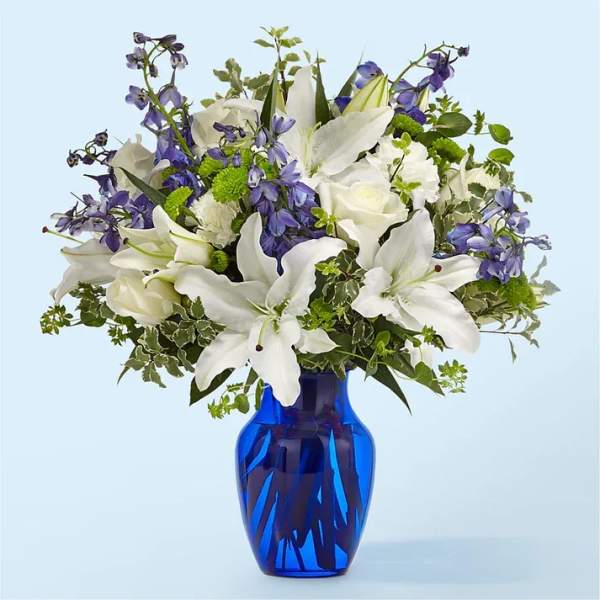 White lilies and purple flowers in a blue glass vase