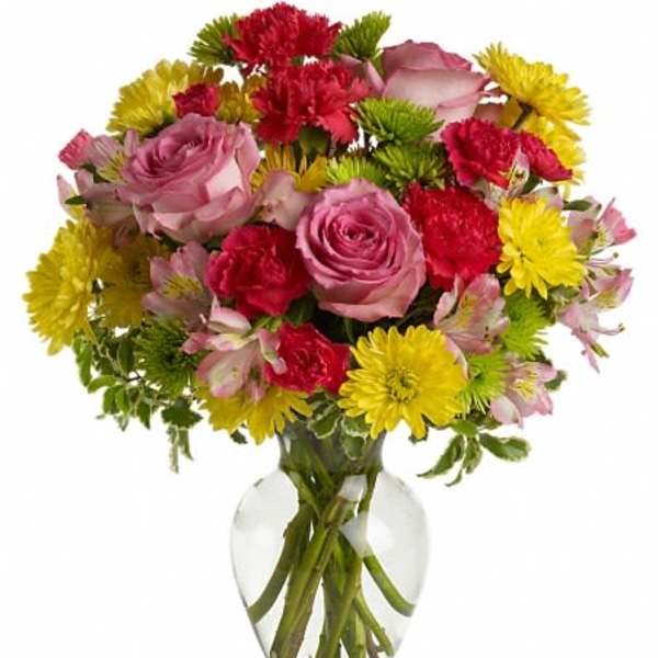 Mixed bouquet of pink roses, red carnations, and yellow daisies in a clear glass vase