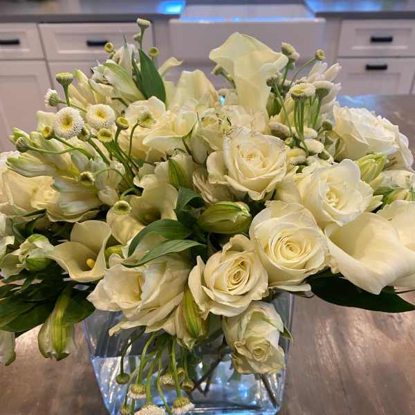 White roses and calla lilies arranged in a clear square vase