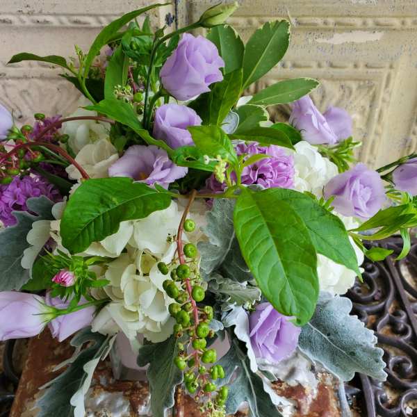 Lavender and white floral arrangement with greenery in a container