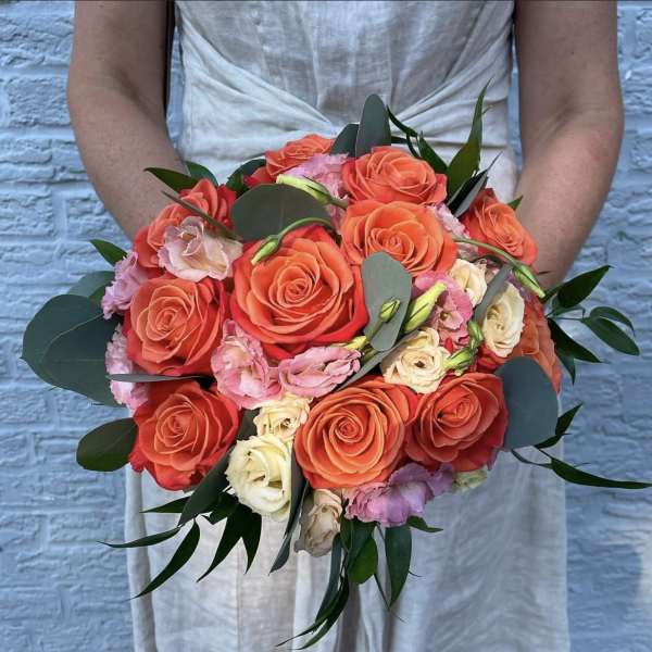 Handheld bouquet of coral and blush roses with greenery