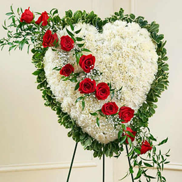 Standing heart-shaped wreath of white flowers with red roses on a metal easel