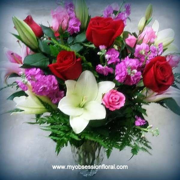 Bouquet of red roses and white lilies with pink filler flowers in a glass vase
