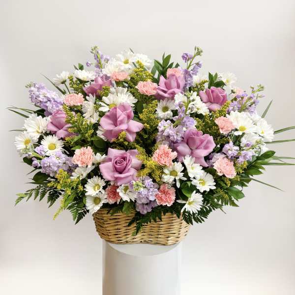 Basket arrangement of pink roses, daisies, carnations, and lavender flowers