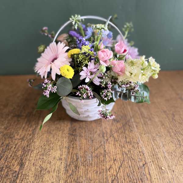 Pastel mixed flower arrangement in a white basket with a handle