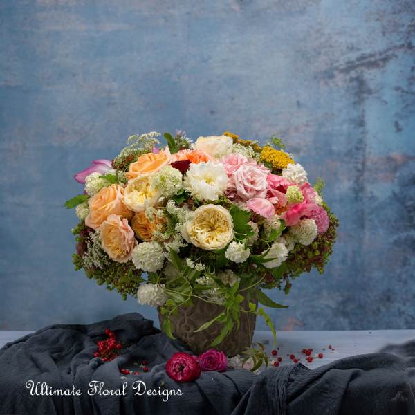 Mixed bouquet of peach, pink, white, and yellow flowers in a decorative vase