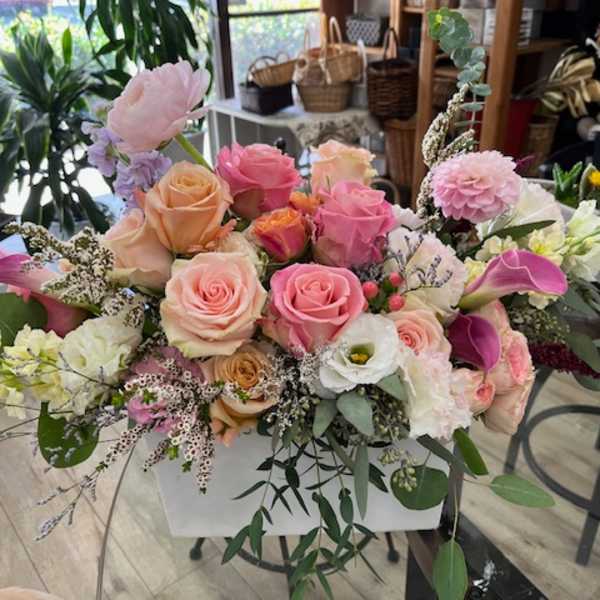 Mixed pastel bouquet with roses, calla lilies, and other blooms in a white container