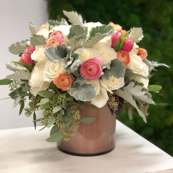 Low arrangement of white roses with pink and peach ranunculus and tulips in a blush cylinder vase