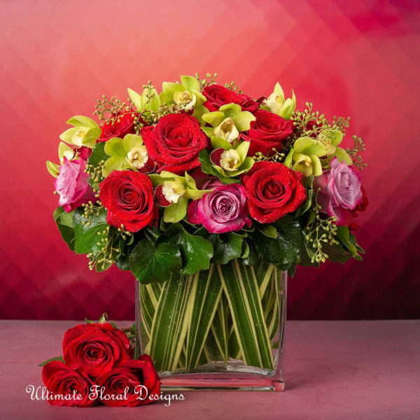 Red and pink roses with green orchids in a glass vase
