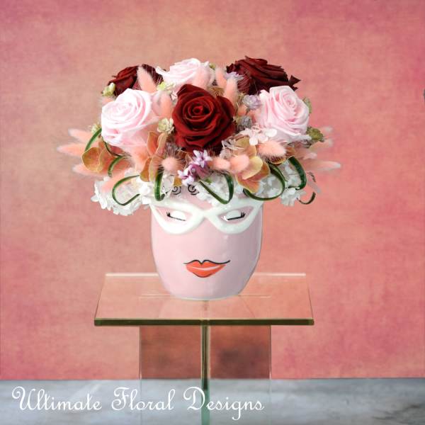 Pink and red rose arrangement in a decorative face vase