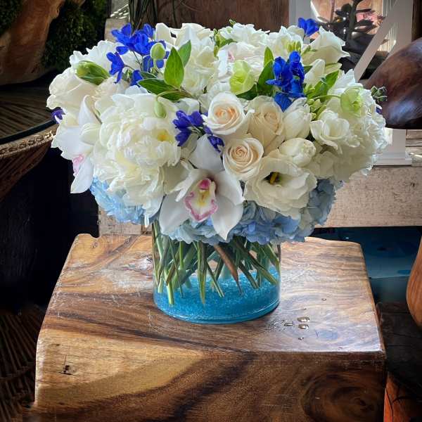 White floral arrangement with blue accents in a clear glass vase