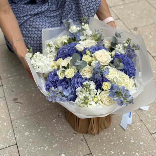 Large bouquet of blue and white flowers wrapped in translucent paper