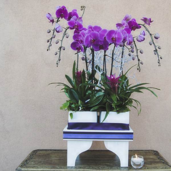 Purple orchid arrangement in a white container with a small candle beside it