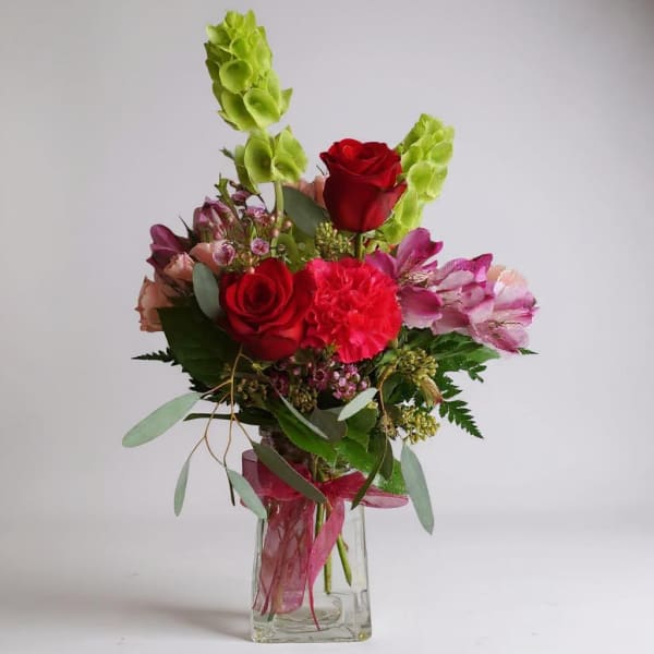 Red roses and pink flowers arranged in a clear glass vase.