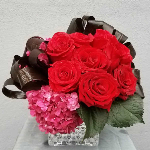 Red roses and pink hydrangeas in a clear square vase