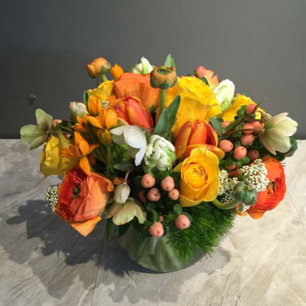 Bright orange and yellow mixed flower arrangement in a glass vase