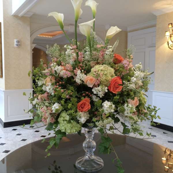 Large floral arrangement with white calla lilies and pink and coral roses in a glass vase
