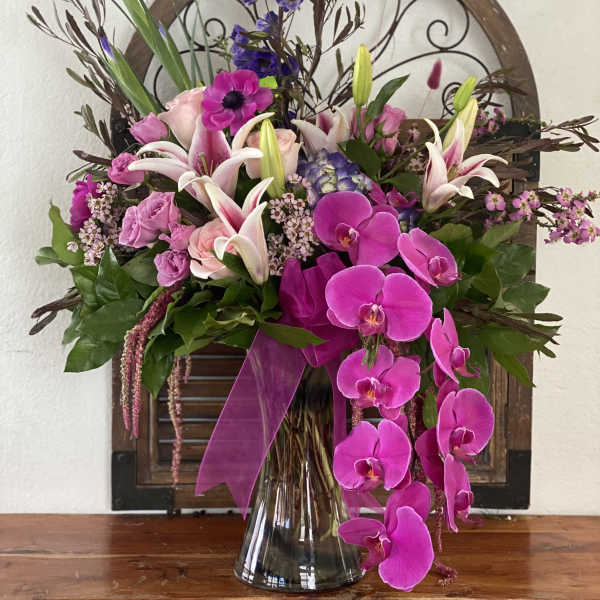 Pink and white floral arrangement in a glass vase with orchids and lilies