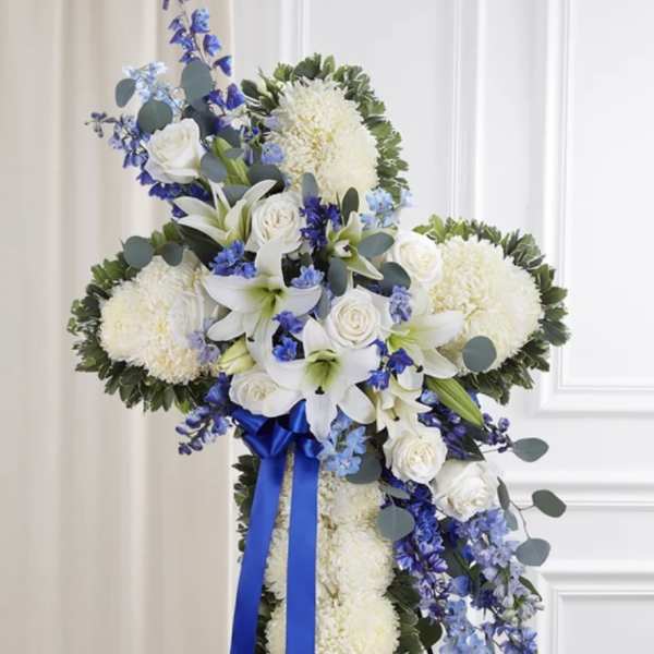 Standing floral cross with white flowers, blue accents, and a blue ribbon