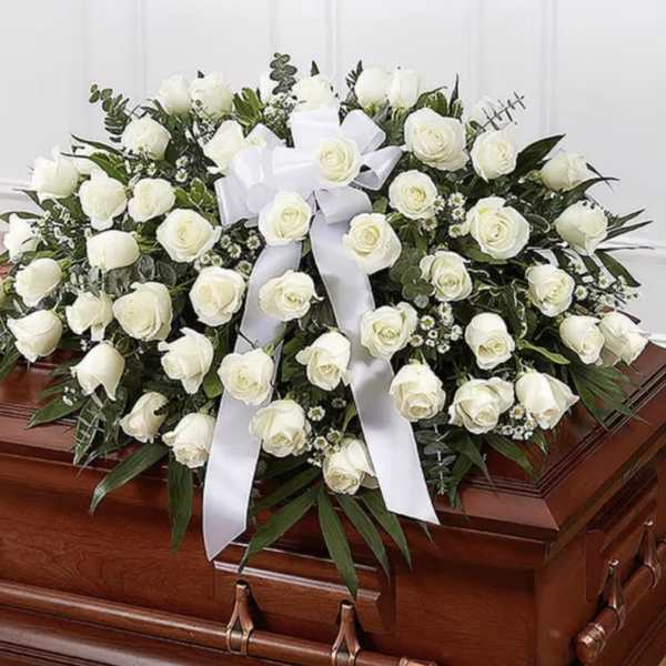 White rose casket spray with a white ribbon on a wooden casket