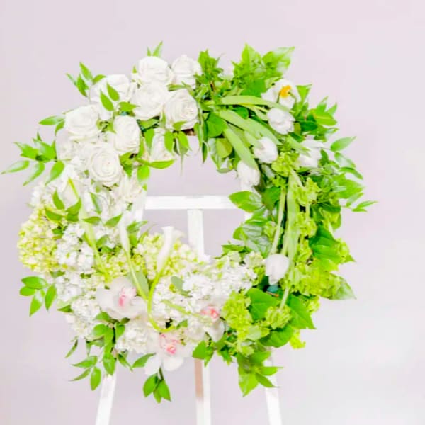 White floral wreath with green foliage on a stand