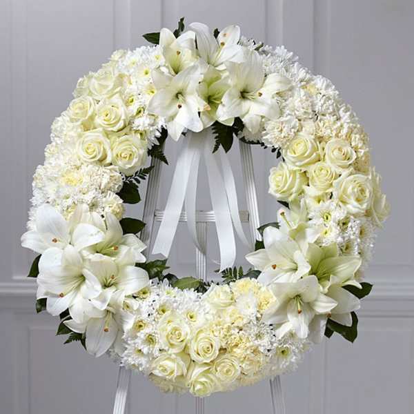 Standing white funeral wreath of lilies, roses, and mums on an easel with white ribbon