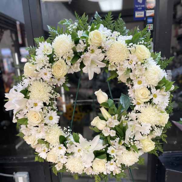 White floral wreath on a stand with roses and daisies