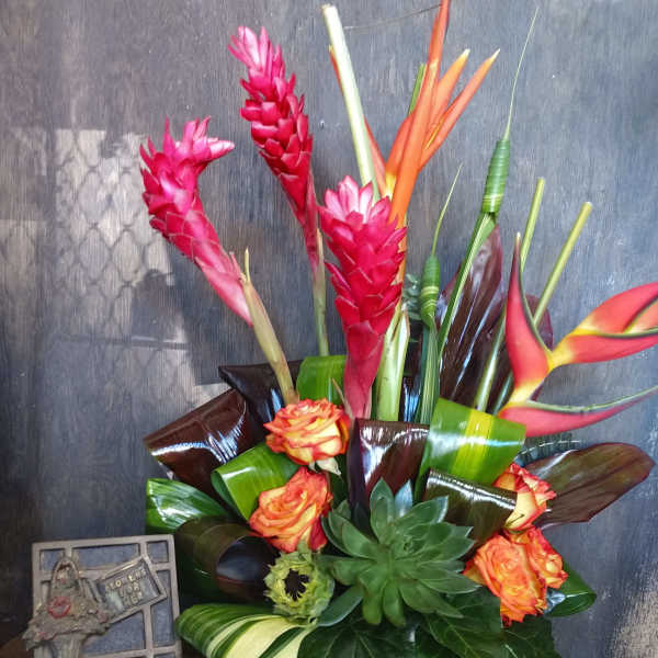 Tropical bouquet with pink ginger, orange heliconia, roses, and succulents in a white vase