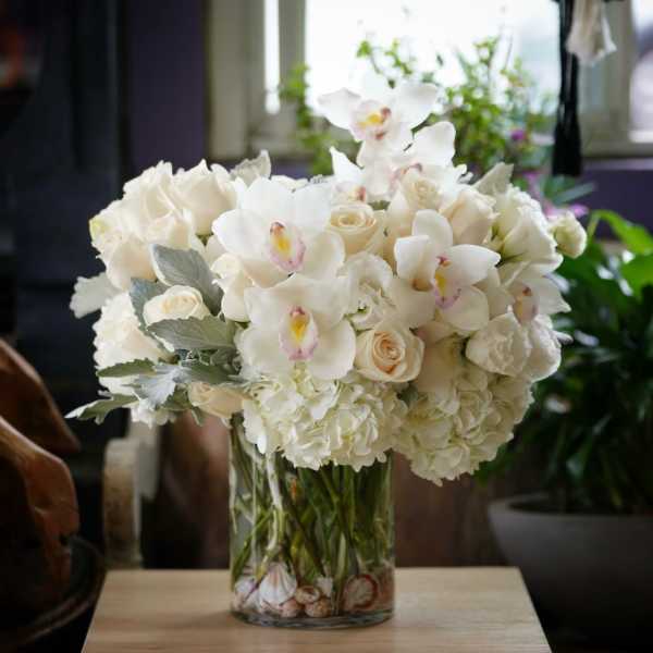 White floral arrangement in a glass vase with orchids and roses