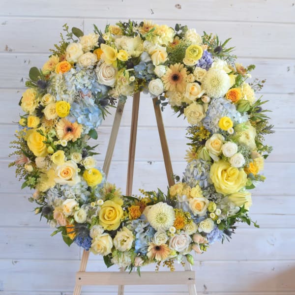 Large floral wreath of yellow, white, and blue flowers on a wooden stand