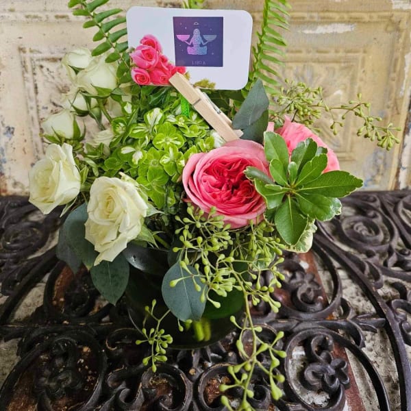 Pink and white roses arranged in a small vase with a Libra card