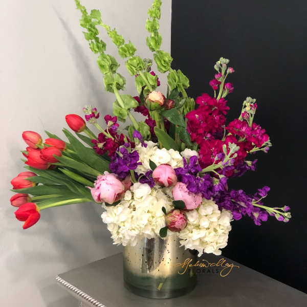 Colorful bouquet with red tulips, pink peonies, white hydrangeas, and purple stock in a metal vase