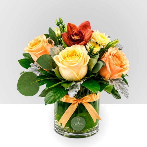Bouquet of peach and yellow roses in a glass vase with a ribbon