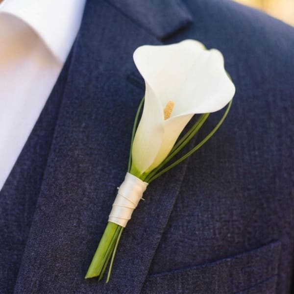 White calla lily boutonniere pinned to a dark suit jacket