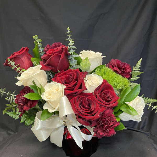 Red and white rose bouquet in a dark vase with a white ribbon