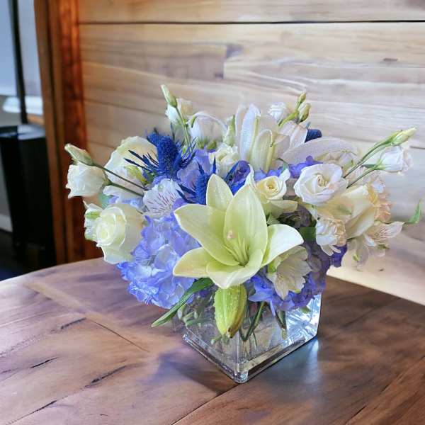 White lilies and blue hydrangeas in a square glass vase