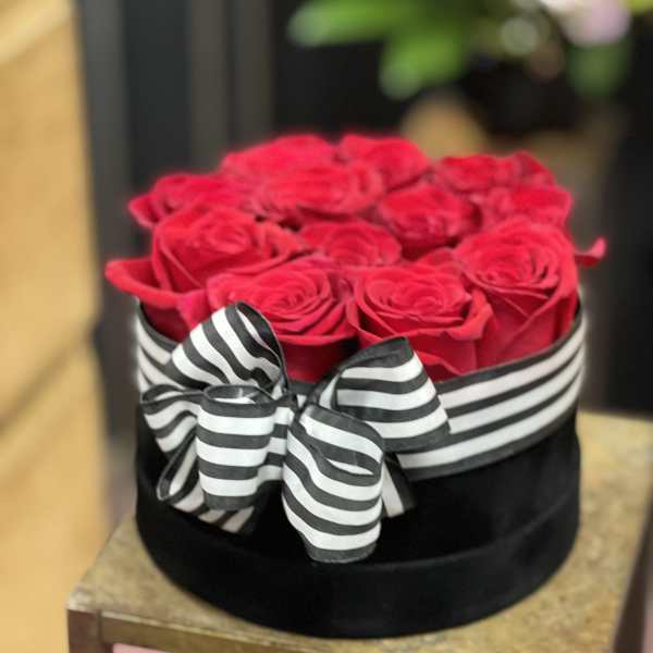 Red roses in a black hat box with a black-and-white striped bow