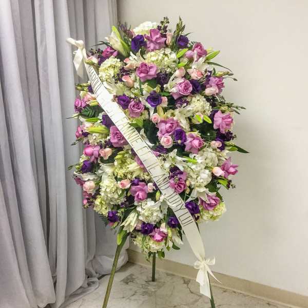 Large standing floral spray in purple, pink, and white with a ribbon
