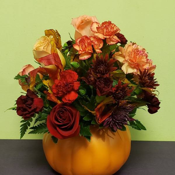 Autumn floral arrangement in a pumpkin-shaped container with roses and carnations