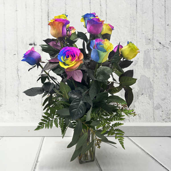 Rainbow-colored roses in a clear glass vase with dark foliage