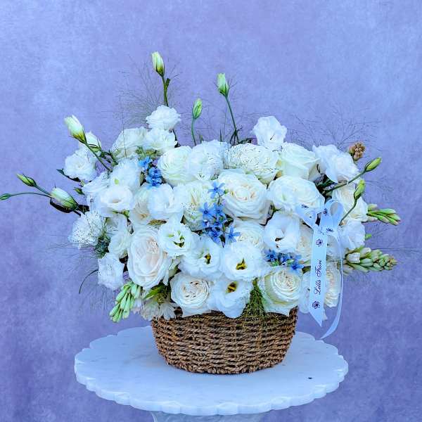 White floral arrangement in a woven basket with a ribbon bow