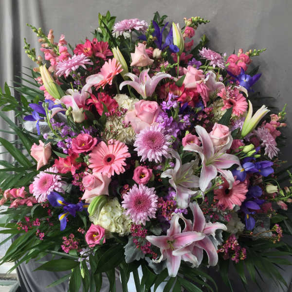 Large mixed bouquet with pink lilies, roses, and purple flowers in a white vase