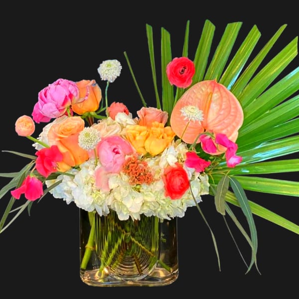 Colorful mixed bouquet in a clear glass vase with palm fronds