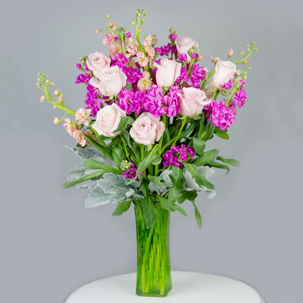Pink roses and purple flowers in a tall green glass vase
