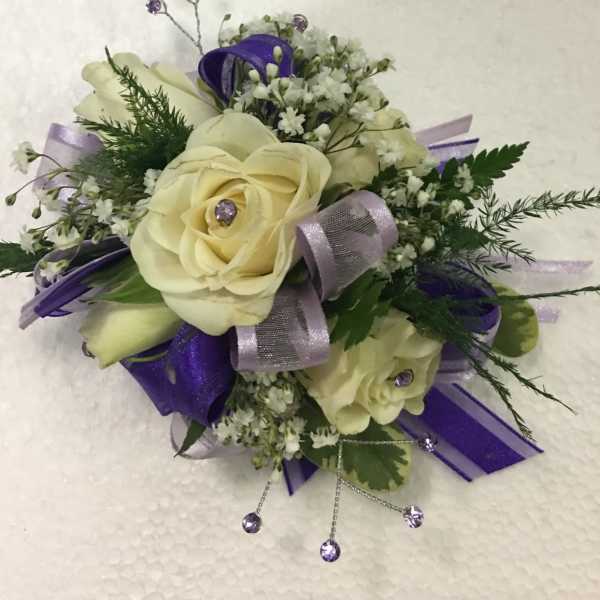 Cream rose corsage with purple ribbon and small white filler flowers